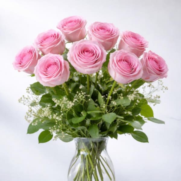 Arrangement of pink roses with white filler flowers in a clear glass vase