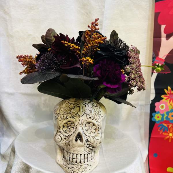 Dark floral arrangement in a decorative skull vase