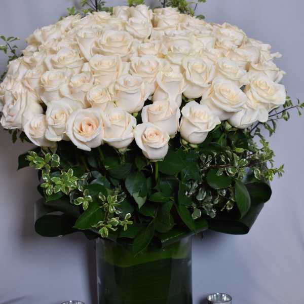Large arrangement of ivory roses with decorative foliage in a clear glass cylinder vase.