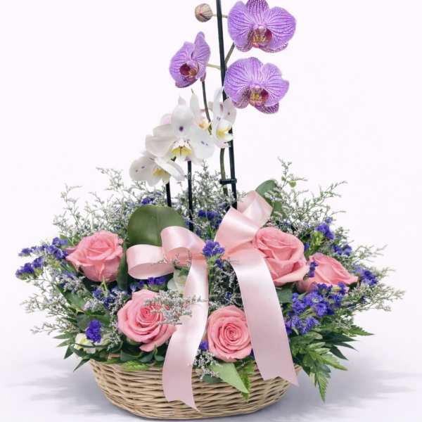 Basket arrangement with pink roses and purple orchids tied with a pink ribbon