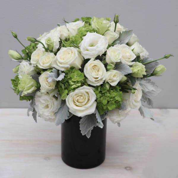 White rose bouquet in a black vase with green accents