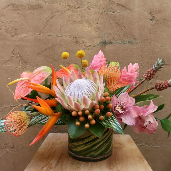 Tropical flower arrangement in a green glass vase with pink and orange blooms