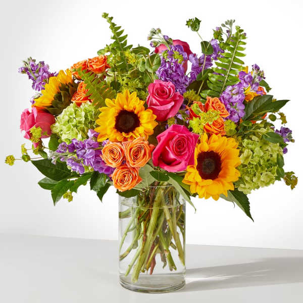 Mixed bouquet of roses, sunflowers, and purple blooms in a glass vase