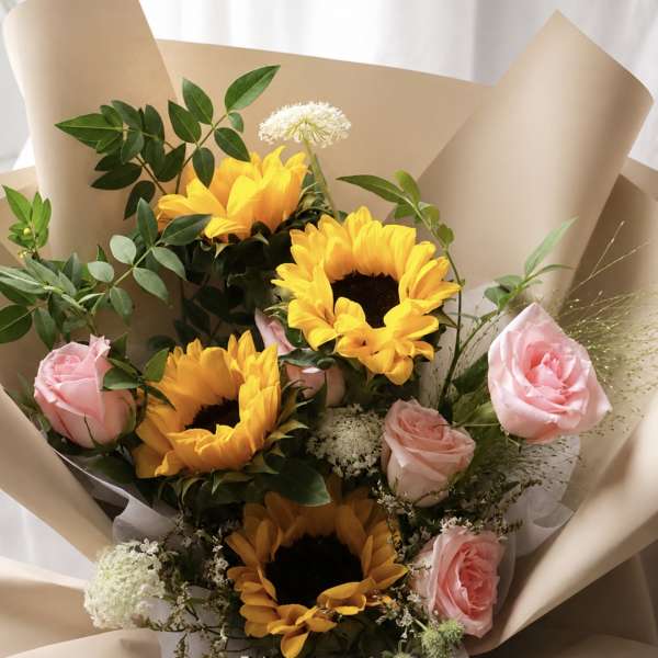 Bouquet of sunflowers and pink roses wrapped in beige paper