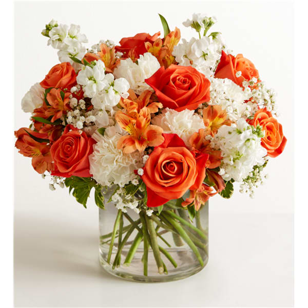 Orange roses and white flowers arranged in a clear glass vase