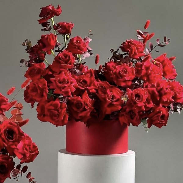 Red rose arrangement in a red cylindrical vase on a white pedestal