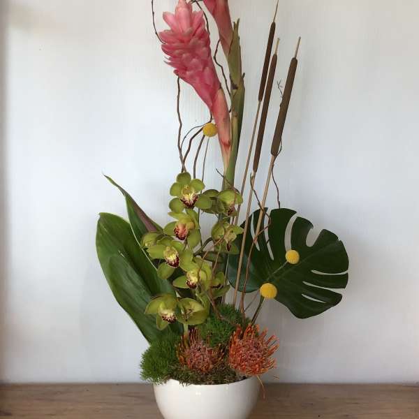Tall tropical arrangement with pink blooms in a white vase