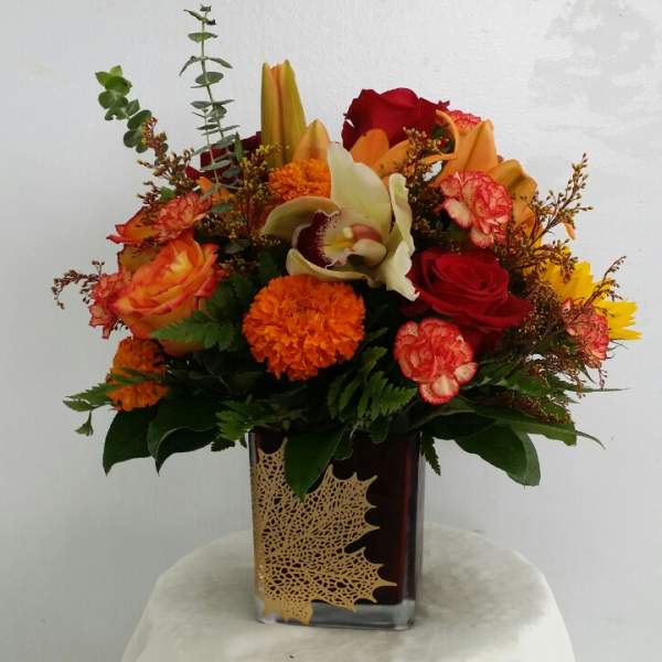 Mixed bouquet in a square glass vase with red, orange, and yellow flowers