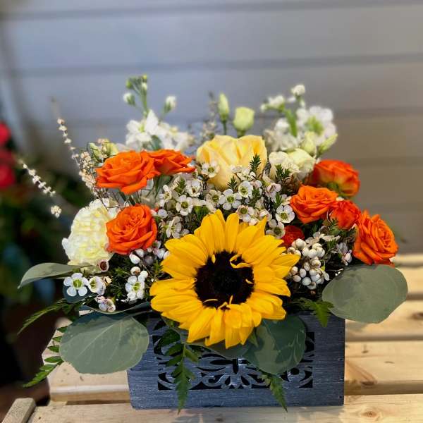 Orange roses and a yellow sunflower in a dark wooden box