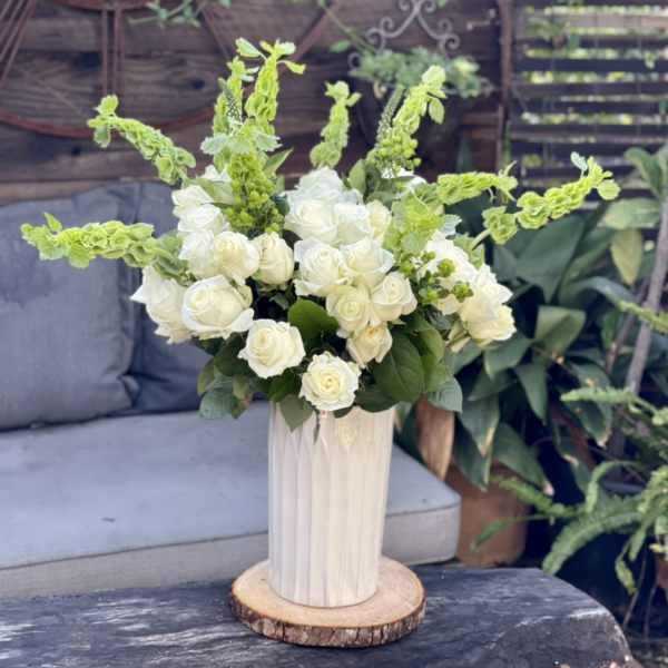 White roses and green spikes arranged in a tall vase