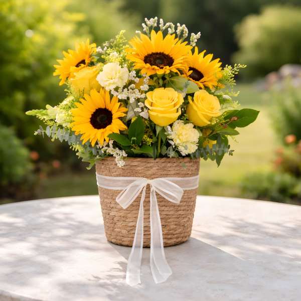 Yellow sunflowers and roses in a woven basket with a white ribbon