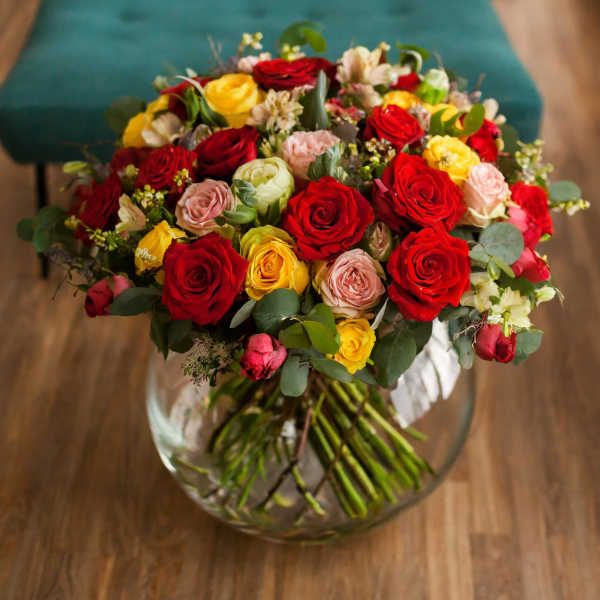 Bouquet of red, yellow, and pink roses in a clear glass vase