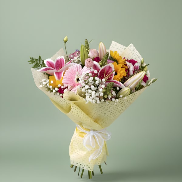 Mixed bouquet of pink, yellow, and white flowers wrapped in pale yellow paper