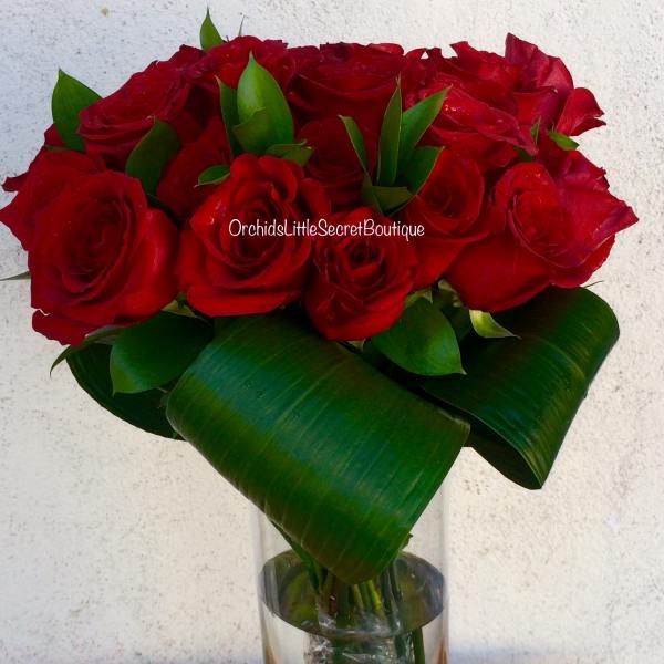 Red roses arranged in a clear glass vase with broad green leaves