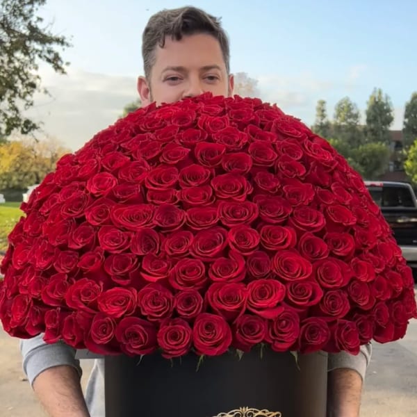 Large dome arrangement of red roses in a black hat box held by a person