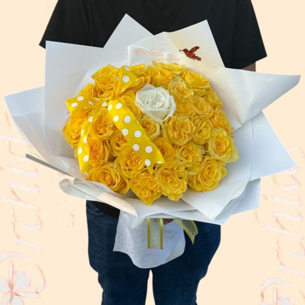 Bouquet of yellow roses wrapped in white paper with a polka-dot ribbon