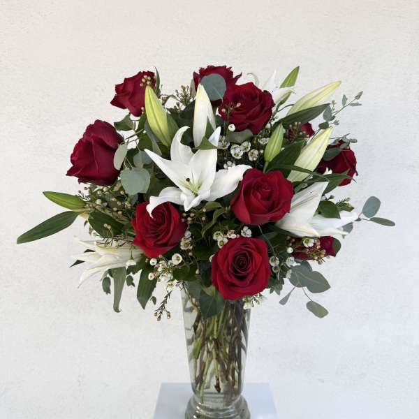 Tall arrangement of red roses and white lilies in a clear glass vase