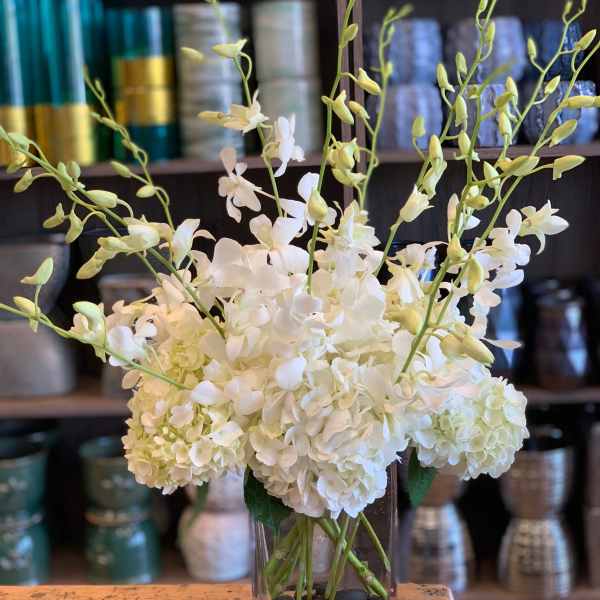 White hydrangeas and orchid stems in a clear glass vase
