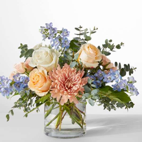 Mixed bouquet of roses, chrysanthemum, and blue flowers in a glass vase
