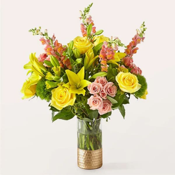 Bouquet of yellow roses, pink spray roses, and lilies in a glass vase