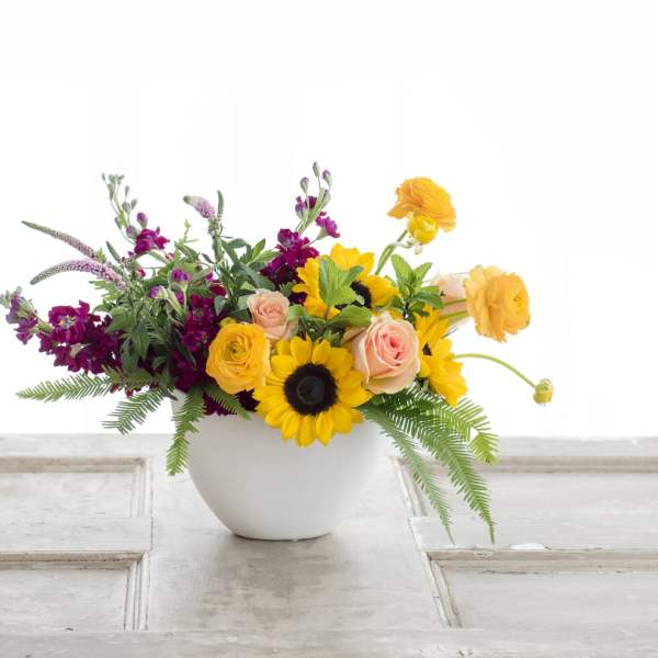 Mixed bouquet in a white vase with sunflowers, roses, and orange blooms