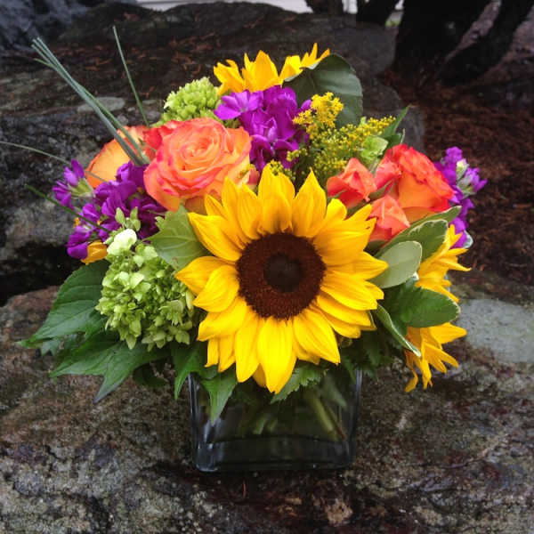 Bouquet of sunflowers, orange roses, and purple flowers in a glass vase