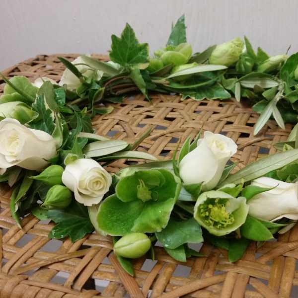 White rose and green flower crown on a woven surface