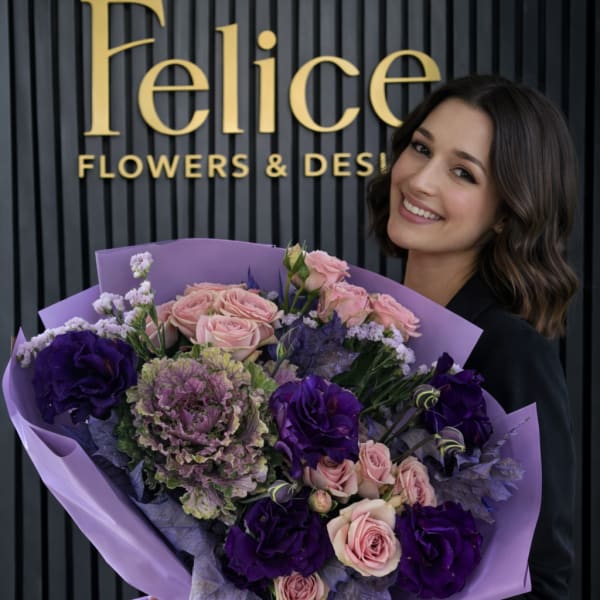 Woman holding a large bouquet of pink and purple flowers wrapped in lavender paper