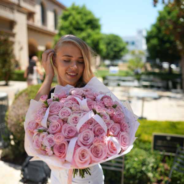 Woman holding a large bouquet of pink roses wrapped in white paper