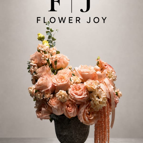 Peach floral arrangement in a dark vase with ribbon and trailing accents