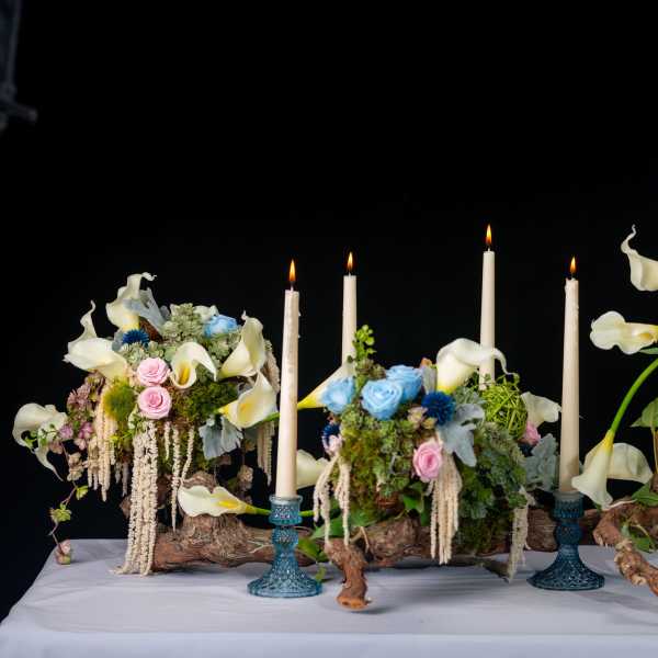Three floral arrangements with white calla lilies and candles on driftwood bases