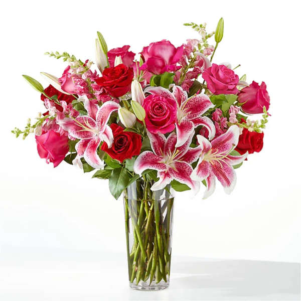 Bouquet of pink and red roses with pink lilies in a clear glass vase
