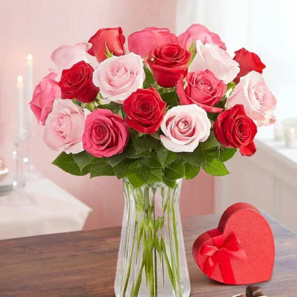 Bouquet of red and pink roses in a clear glass vase with a heart-shaped gift box