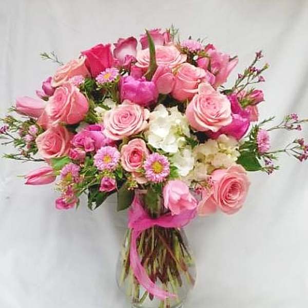 Pink roses and small white flowers in a glass vase with a pink ribbon