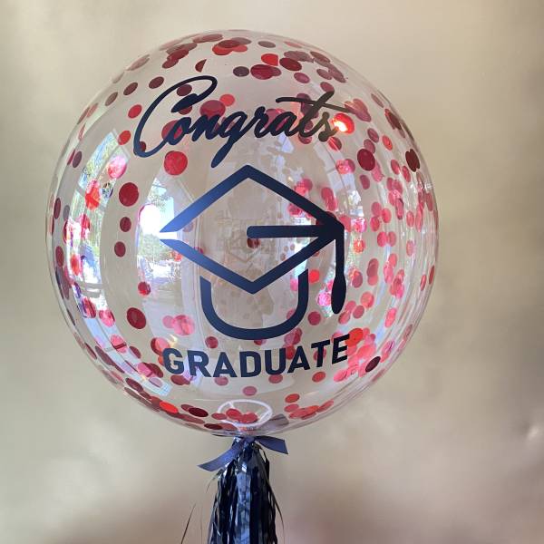 Clear balloon with pink confetti and "Congrats Graduate" text on a stand
