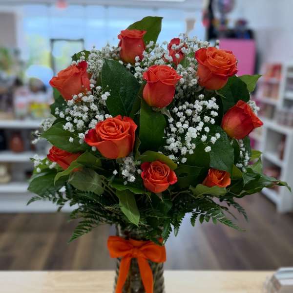 Orange roses in a glass vase with baby's breath and a ribbon