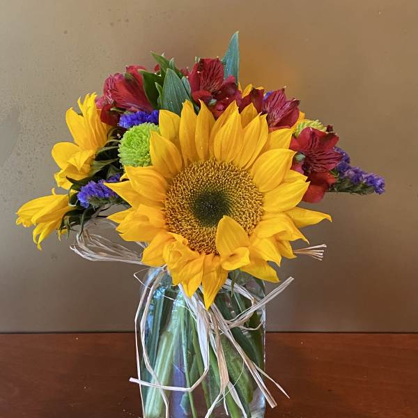 Sunflower bouquet with mixed red and purple flowers in a glass vase