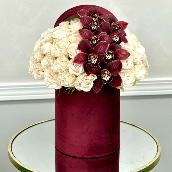 Cream hydrangeas and burgundy orchids in a velvet hat box