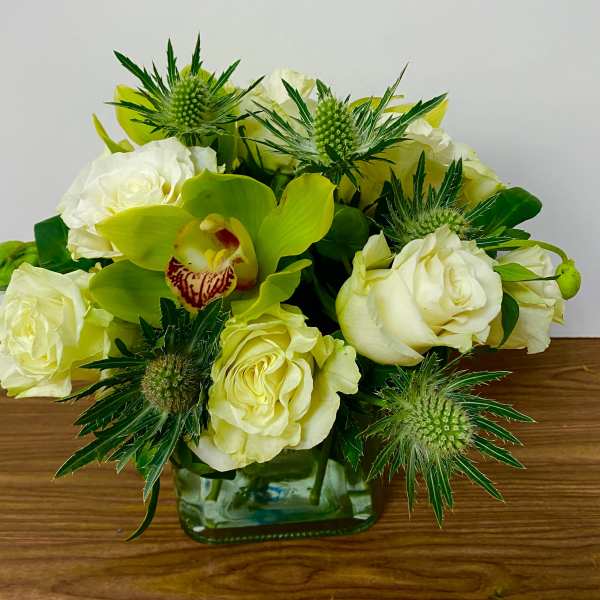 White roses and a green orchid arranged in a square glass vase