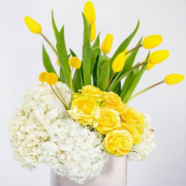 Yellow tulips and roses arranged with white hydrangeas in a tall vase