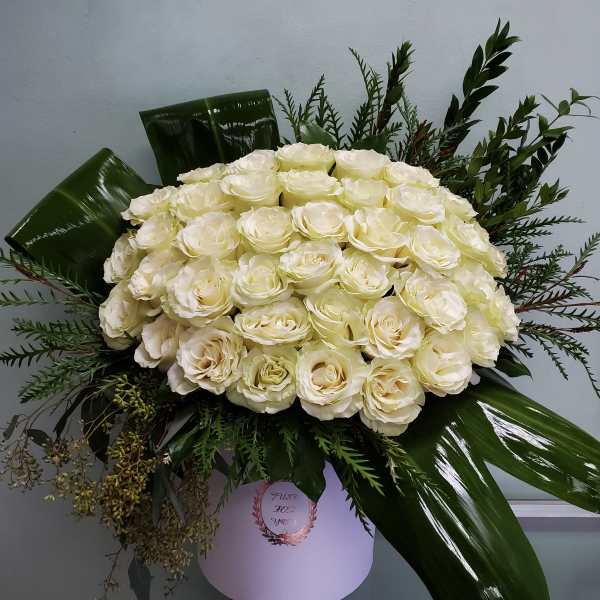 Large bouquet of cream roses with dark green foliage in a white box