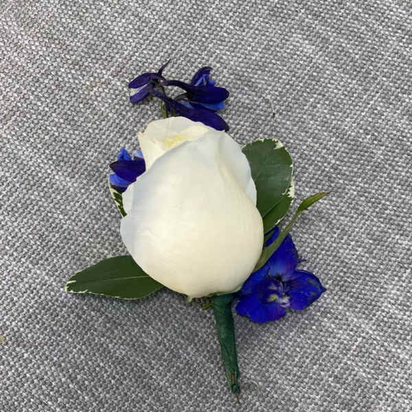 White rose boutonniere with blue accent flowers on gray fabric