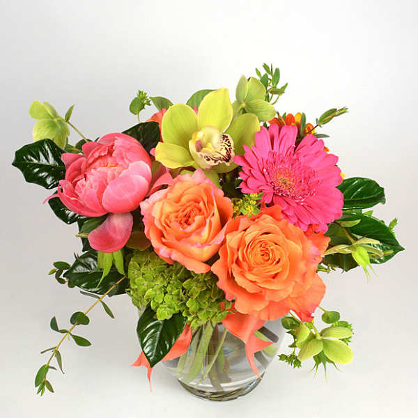 Bouquet of orange roses, pink gerbera daisies, and green orchids in a glass vase