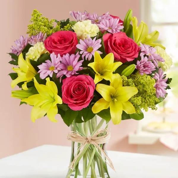 Bouquet of pink roses, yellow lilies, and lavender daisies in a glass vase