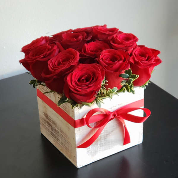 Red roses arranged in a white wooden box with a red ribbon