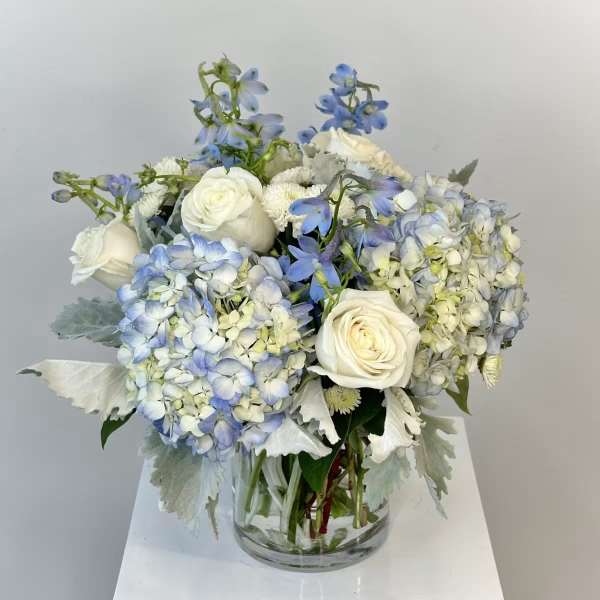 White roses and blue hydrangeas in a clear glass vase