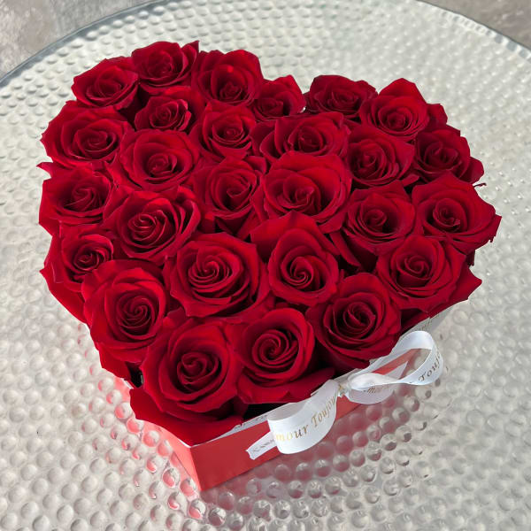 Heart-shaped box filled with red roses and tied with a white ribbon on a glass table