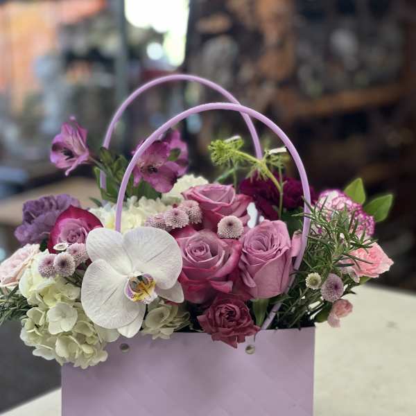 Pink and white floral arrangement in a lavender gift bag