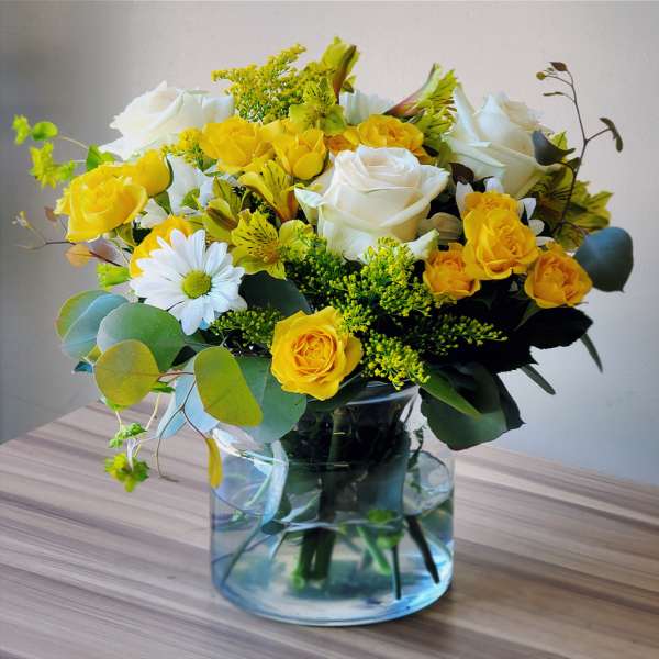 Yellow and white roses in a clear glass vase with a daisy