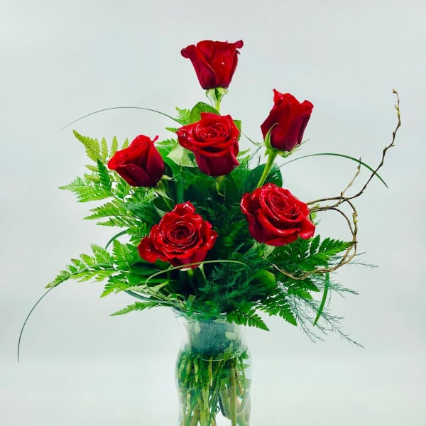 Red roses arranged in a clear glass vase with green foliage